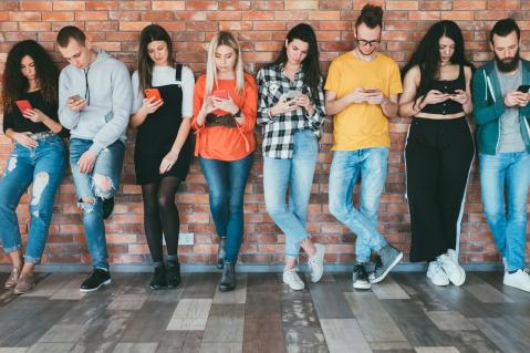 Junge Leute in einer Reihe, alle schauen auf Smartphones zu Artikel: Messenger Dienste - worauf Sie bei der Auswahl achten sollten