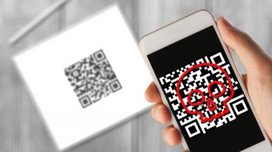 Hintergrund: Tablet mit QR-Code, vorne von Smartphone gescannter QR-Code mit rotem Totenkopf