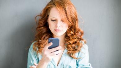 Frau hält Smartphon in der Hand und schaut es mit fragendem Blick an