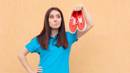 Frau hält  rote Turnschuhe in der Hand und macht ein kritisches Gesicht