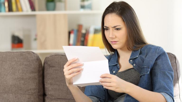 Junge Frau auf Sofa mit Brief in Hand, schaut irritiert