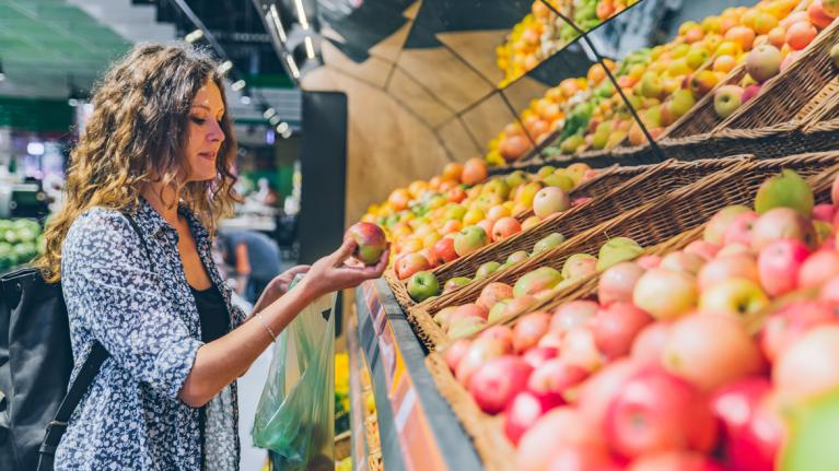 Frau vor Regal mit Äpfeln im Supermarkt