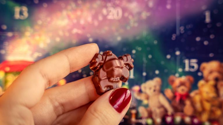 Nahaufnahme Hand mit Schokolade aus Adventskalender, im Hintergrund bunter Adventskalender