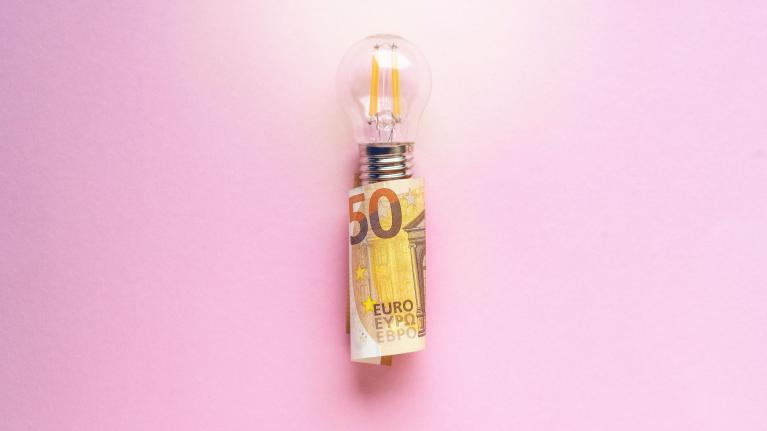 Glühbirne in 50 Euro Schein gewickelt auf rosa Hintergrund