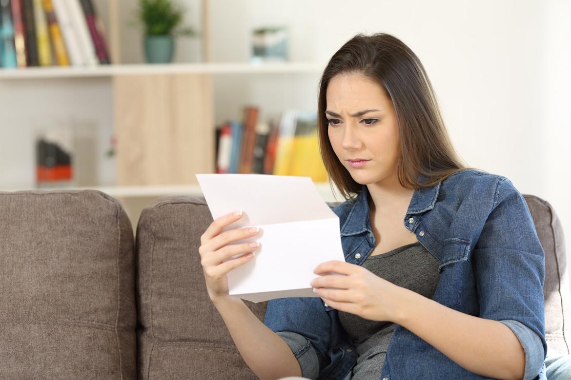 Junge Frau auf Sofa mit Brief in Hand, schaut irritiert