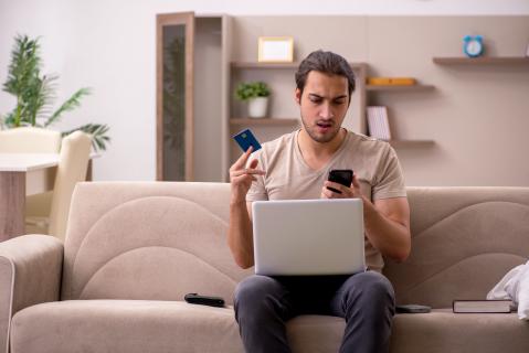 Mann erschrocken mit Kreditkarte vorm Rechner beim Onlineshopping